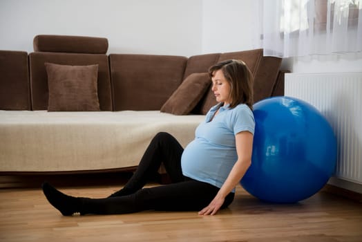 Pregnant woman relaxing after exercising with fit ball at home