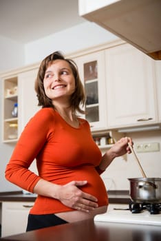 Lifestyle portrait of smiling pregnant woman cooking in kitchen, looking away