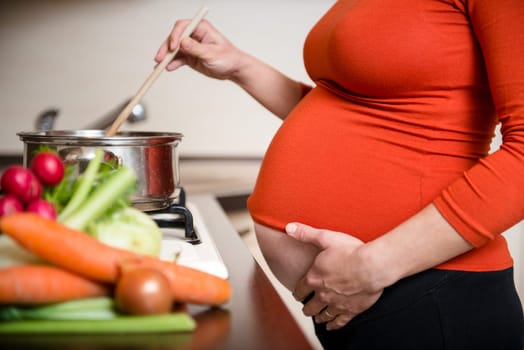 Crop of belly - pregnant woman cooking vegetables in kitchen