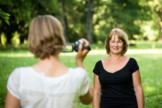 Woman is taking video of her senior mother in nature with camcorder