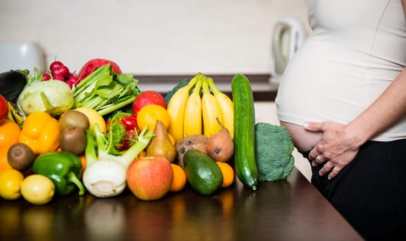 Detail of pregnant woman (belly) with abundance of vegetables and fruits