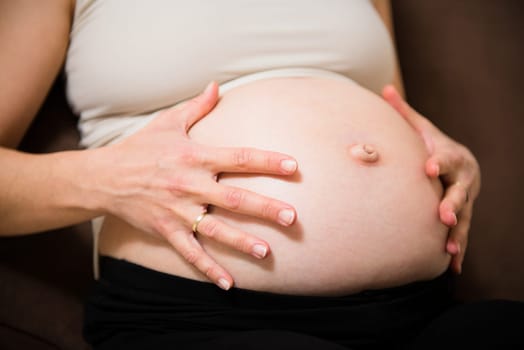 Detail of hands holding pregnant belly - indoors