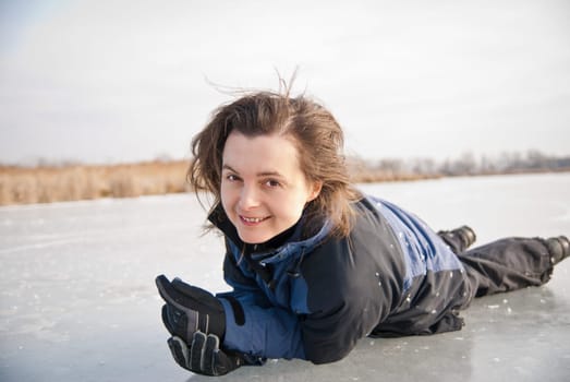 Young smiling woman is lying on ice (frozen lake) - winter outdoor scene