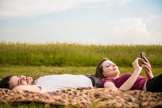 Young couple relaxing outdoor in nature - woman with smartphone lies on man