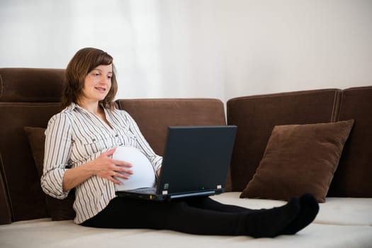 Pregnant woman working on laptop from home on sofa
