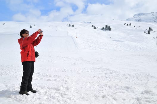 Senior woman taking picture with camera in mountain winter snow landscape