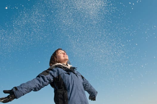 Young woman throwing snow on blue sky in background - joy and happines emotions