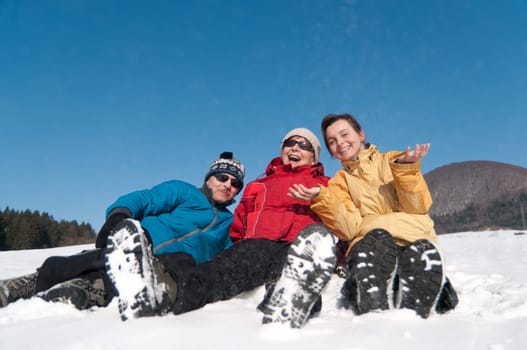 Family portrait - senior man and woman with their adult daughter in winter - sitting in snow