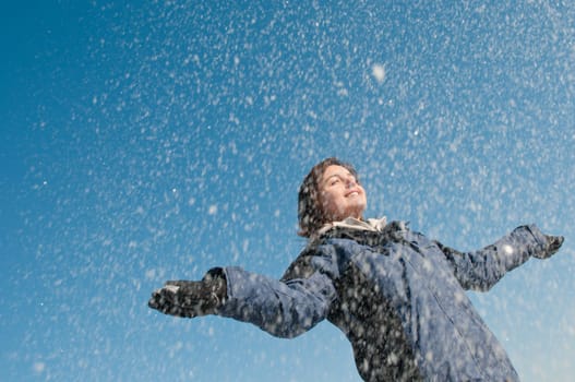 Young woman throwing snow on blue sky in background - joy and happines emotions