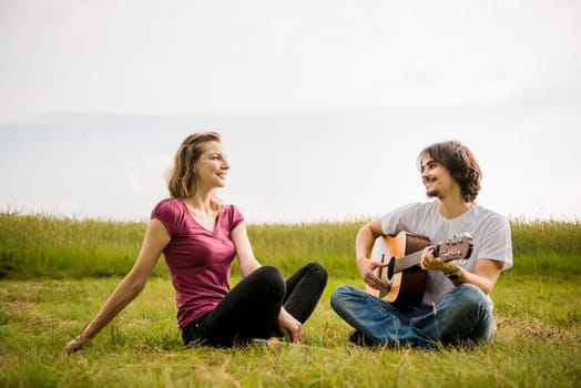 Young man playing guitar to his girlfriend in nature - dating couple