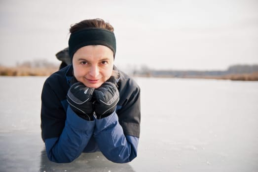 Young smiling woman is lying on ice (frozen lake) - looking away