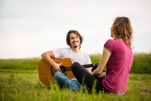 Young man playing guitar to his girlfriend in nature - dating couple