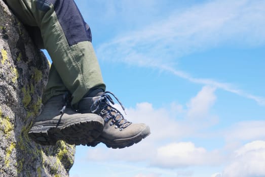 Legs of hiker hang from rock when relaxing with blue sky