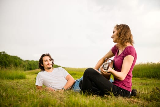Young woman playing to his boyfriend on guitar - dating couple outside in nature