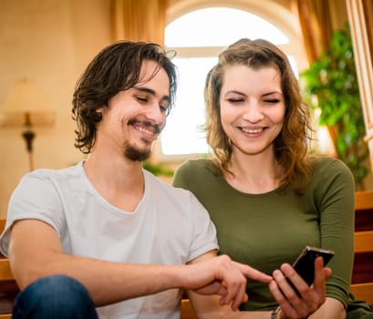Young happy couple looking on smartphone display - indoors