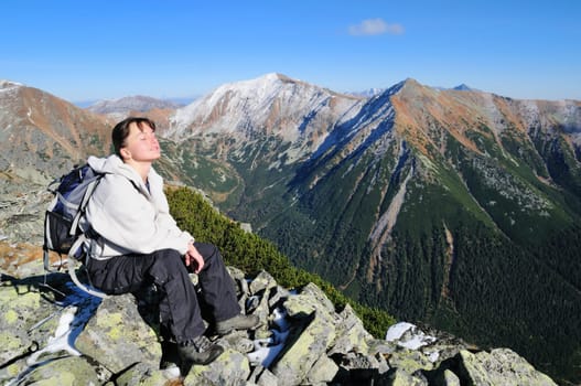 Hiker relaxing on rocky hill with clear blue sky with face turned to sun
