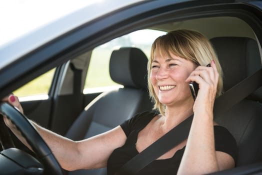 Lifestyle photo of attractive senior woman driving car and calling with mobile phone
