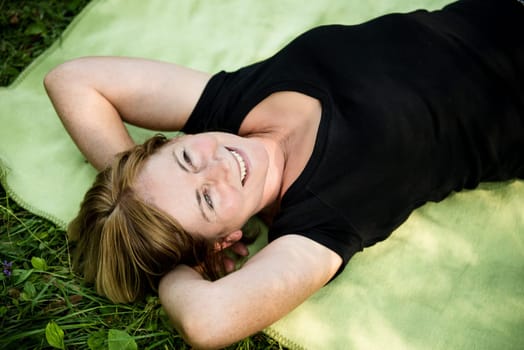 Smiling attractive senior woman lying outdoor on rug in nature