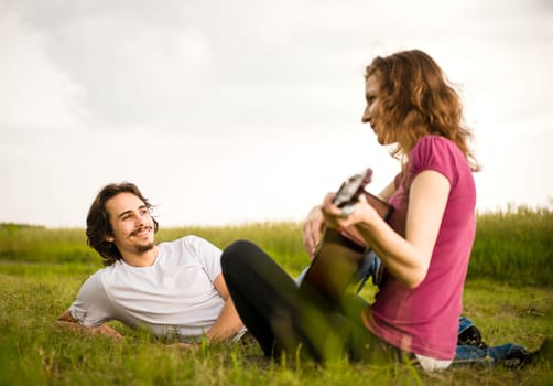 Young woman playing to his boyfriend on guitar - outside in nature