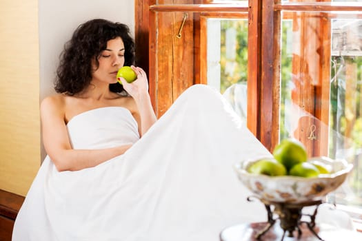 Pretty woman smells green apple on wooden sill