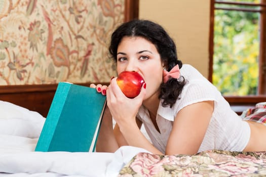 Pretty woman bite red ripe apple at bed