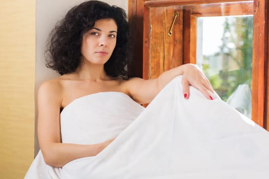 Pretty woman sit near window covered by bed blanket