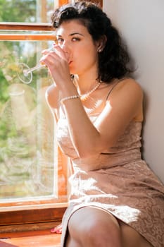 Pretty woman drinking wine from glass on sill