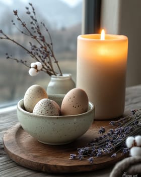 A calming display of speckled eggs resting in a bowl beside a lit candle and lavender flowers. The tranquil atmosphere is enhanced by a scenic view outside the window.