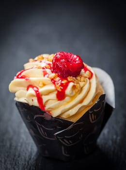 Delicious vanilla cupcake with raspberry on black background