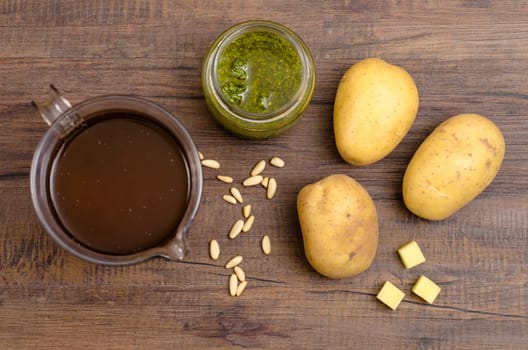 Vegetable broth,pesto,pine nuts and potatoes on a wooden table