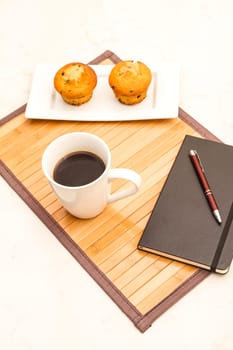 Vanilla with chocolate chips Muffins on a white plate with  a cup of coffee meanwhile taking notes.