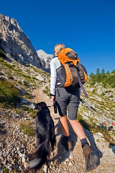 Young woman with dog on a sunny day hiking in high mountains