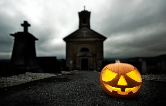 A glowing Jack O Lantern in a dark mist graveyard on Halloween
