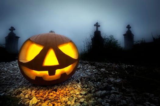 A glowing Jack O Lantern in a dark mist graveyard on Halloween