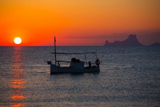 Ibiza sunset Es Vedra view and menorquina fisherboat from Formentera orange sky