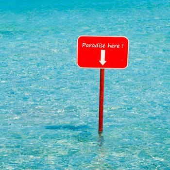 Aqua turquoise tropical sea water with red sign saying Paradise here