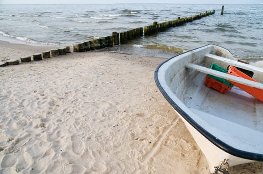 Frontal wide-angle shot of a small fishing boat on a white sandy beach with groyne in the background