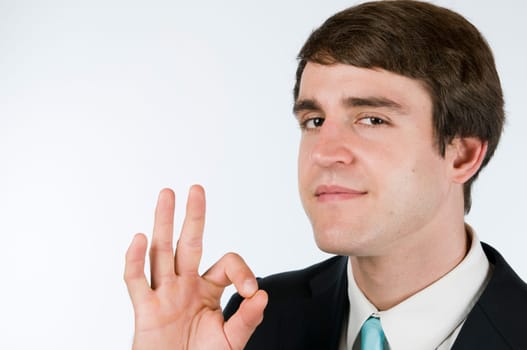 Head-and-shoulder portrait of a young man in a black suit against a white background pointing the OK sign to the camera