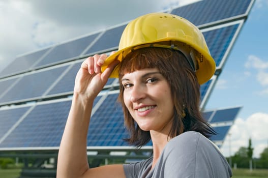 young brunette woman with yellow construction helmet in front of photovoltaic system