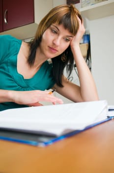 Head-and-shoulder view of a young,brunette woman sitting at the table with pen in hand and binder in front of her