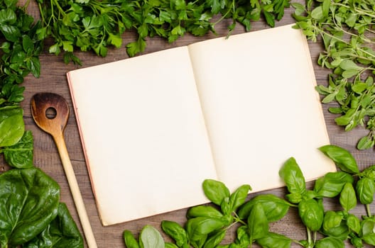 Book by recipe with wooden spoon and green herbs