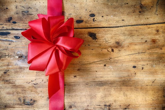 Decorative red ribbon and bow on a rustic wood background with copyspace to celebrate a Merry Christmas, romantic Valentines Day or birthday with a greeting card