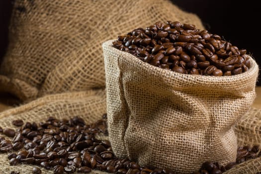 Black roasted coffee beans in a small burlap sack