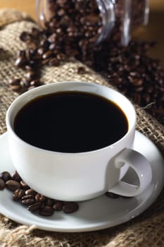 Black roasted coffee beans in a small burlap sack