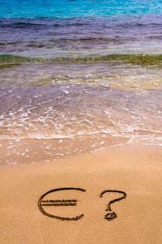 Euro sign in the sand, with blue sea water in background