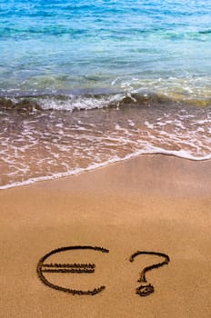 Euro sign in the sand, with blue sea water in background
