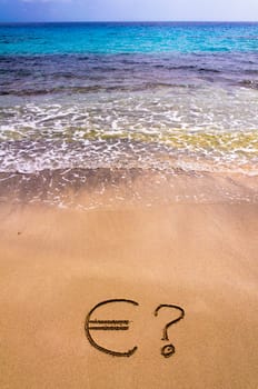 Euro sign in the sand, with blue sea water in background