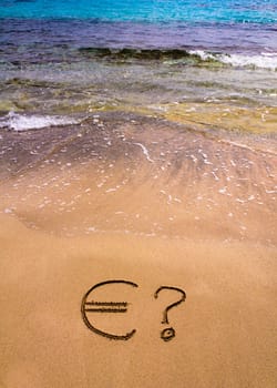 Euro sign in the sand, with blue sea water in background