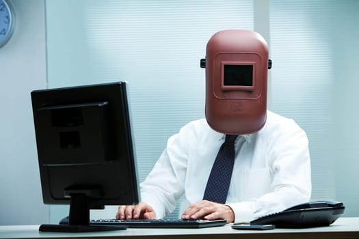 An office worker at his desk wearing a welder's mask