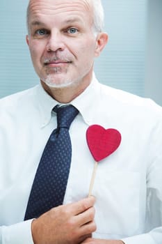 An elegant smiling man with a red heart-shaped toy